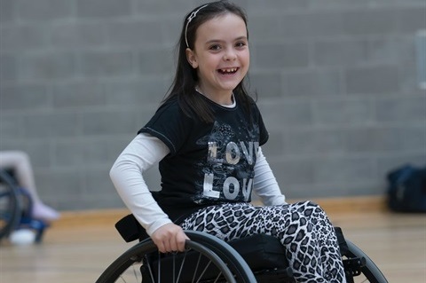 A young girl in a wheel chair smiling